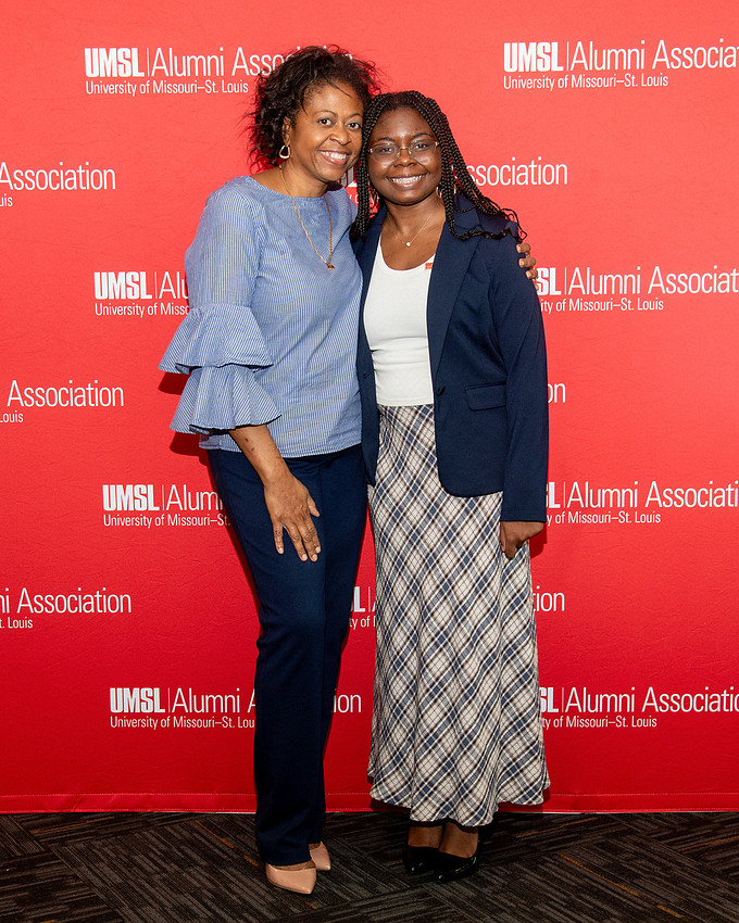 Two guests posing at an UMSL Alumni Association event backdrop