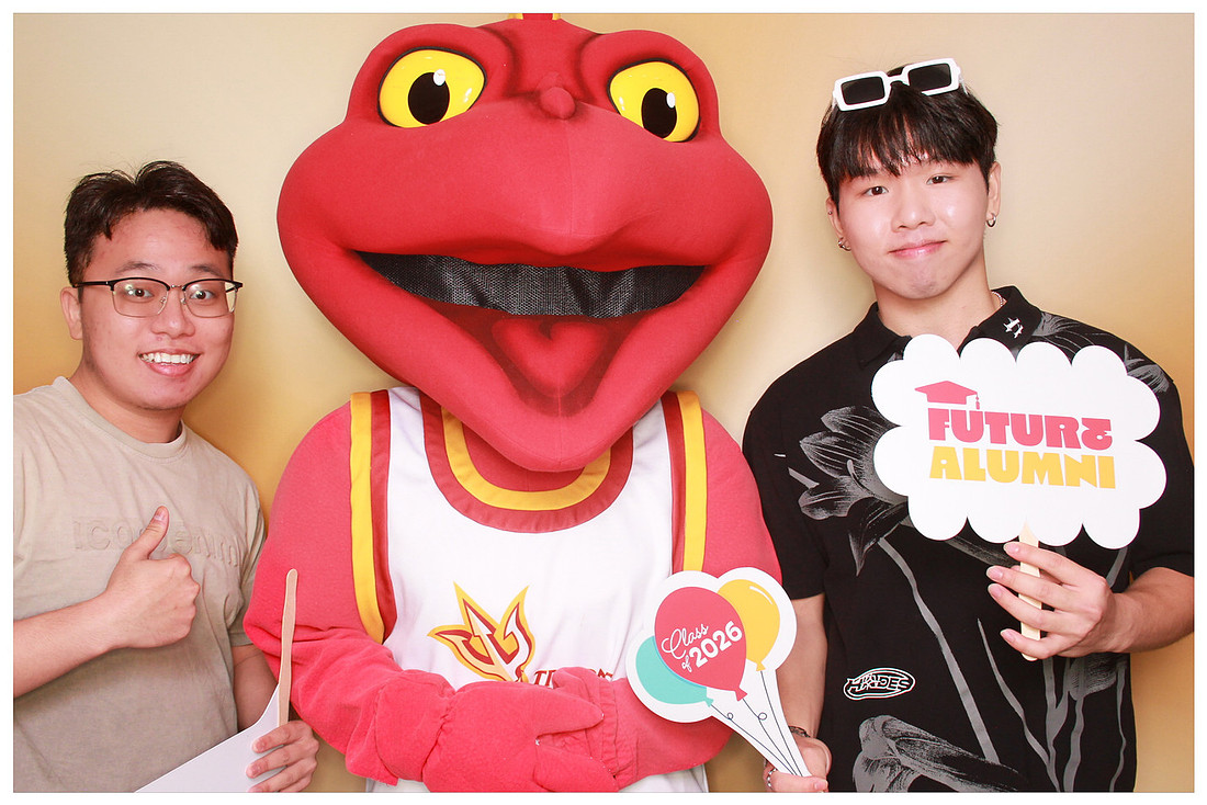 Two guests posing with a red mascot and graduation props