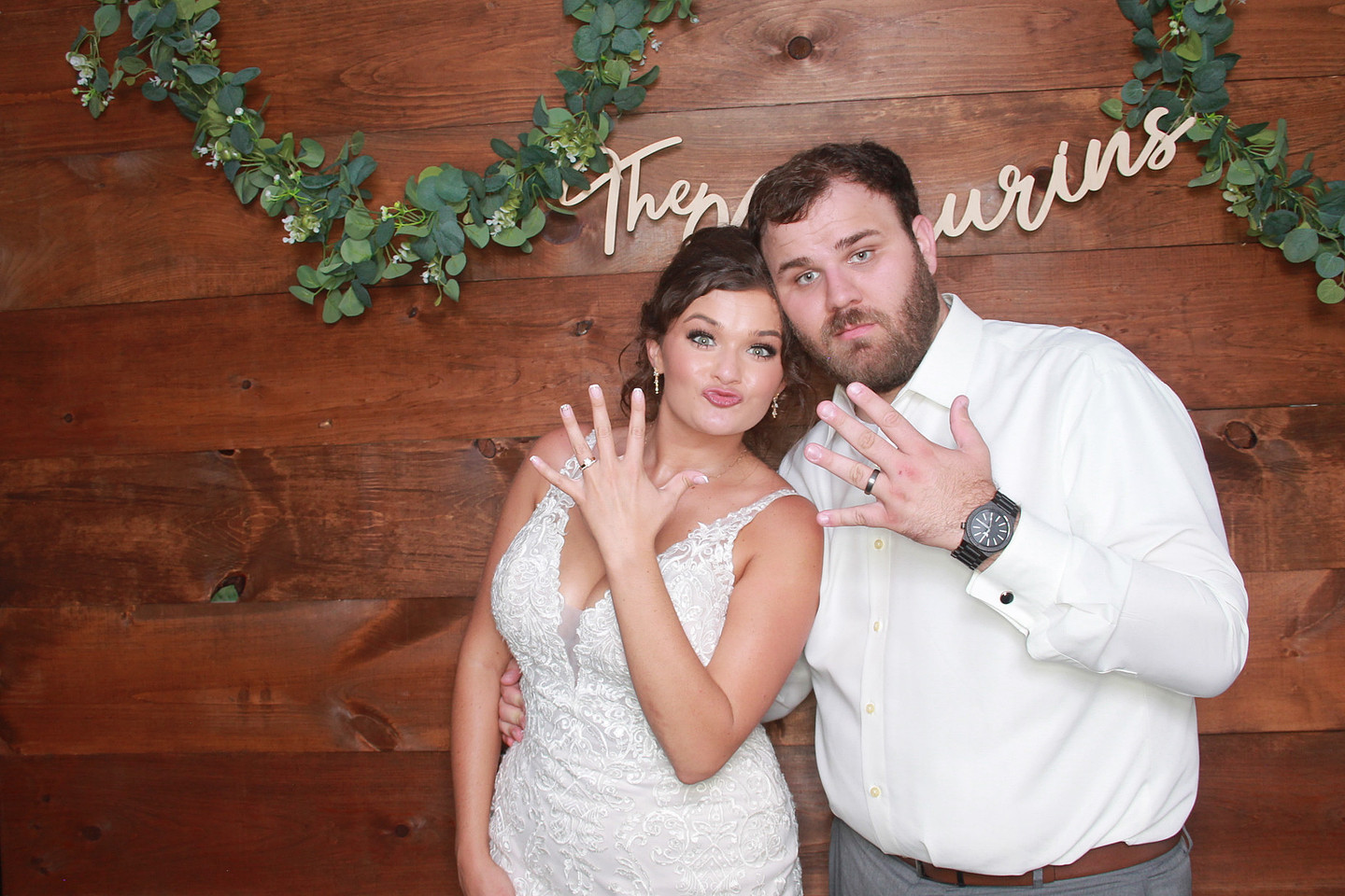 Wedding couple showing their rings in front of a wooden photo booth backdrop