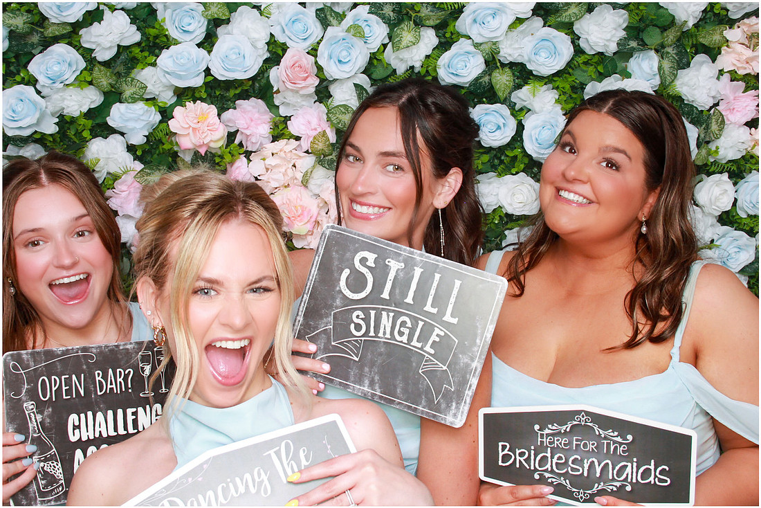 Guests holding playful signs in front of a colorful flower backdrop